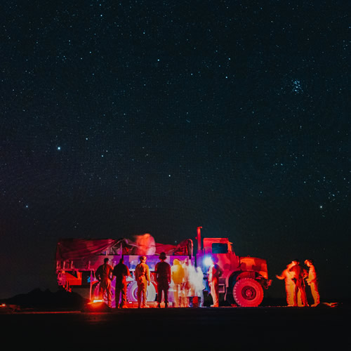 Make it smart. Make it real. | decorative photo featuring a night time shot of a truck with soldiers in front lit by light